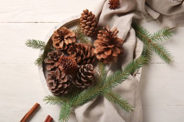 Çam kozalaklı tepsi, köknar dalları ve beyaz ahşap arka planda tarçın