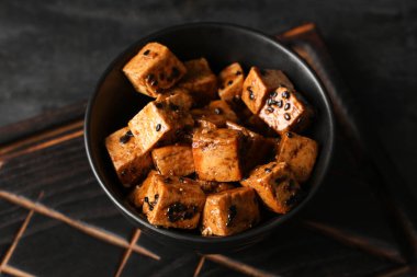 Siyah zemin üzerinde kızarmış tofu peyniri olan bir kase, yakın plan.