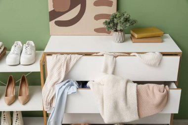 Ayakkabılı raf ünitesi ve dağınık giysiler yeşil duvarın yanındaki tuvalette, yakın plan.