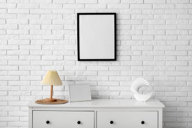 Çekmeceler ve beyaz tuğla duvarda asılı boş bir poster.