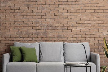 Tuğla duvarın yanında yeşil yastıklı gri kanepe.