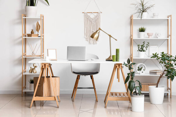 Interior of modern stylish workspace with shelving units and laptop on table