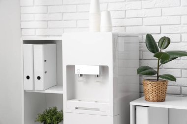 Modern su soğutucusu ve raf üniteleri beyaz tuğla duvarın yanındaki hafif ofiste.