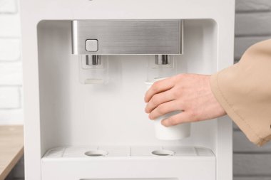 Genç iş kadını modern su soğutucusunu açık ofiste kullanıyor.