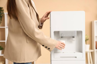 Modern su soğutucusunu şık bir ofiste kullanan genç bir iş kadını.