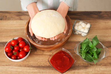 Mutfaktaki ahşap masanın yanında çiğ hamurlu ve pizza malzemeli bir kadın.