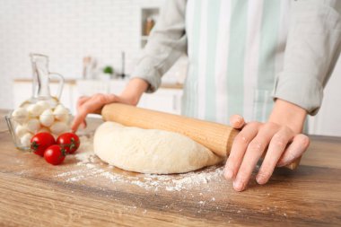 Mutfakta masanın yanında pizza hamuru yuvarlayan bir kadın.