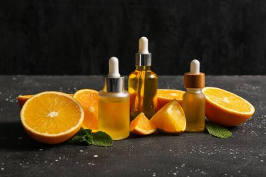 Siyah zemin üzerinde naneli ve taze meyveli portakal yağı şişeleri.