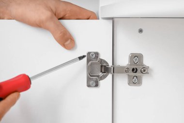 Erkek marangoz dolaba vida sıkıştırıyor. Tornavidayla menteşe, yakın plan.