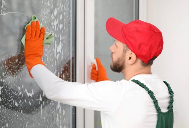 Erkek işçi odada cam yıkıyor.