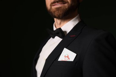Koyu yeşil arka planda Joker poker kartı olan yakışıklı genç adam, yakın plan.