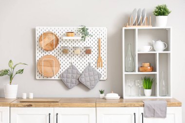 Mutfağın iç tarafındaki beyaz duvarın yanında ev bitkisi ve çatal bıçak bulunan beyaz tezgahlar.