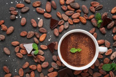 Nane yapraklı bir fincan sıcak çikolata ve siyah grunge arka planda kakao çekirdeği.