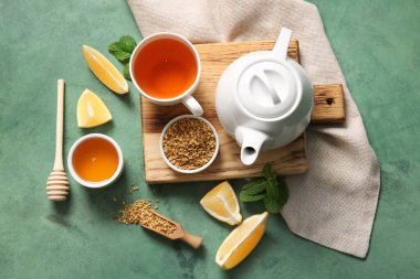 Bir fincan sıcak karabuğday çayı, çaydanlık, limon dilimleri ve ballı yeşil grunge arkaplan.