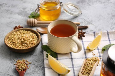 Bir fincan naneli karabuğday çayı, limon dilimleri ve gri grunge arka planda ahşap kepçe.