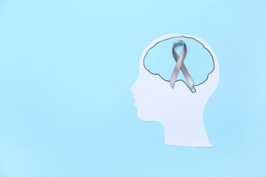 Beyni ve mavi arka planda gri farkındalık kurdelesi olan kağıt insan kafası. Kanser kavramı