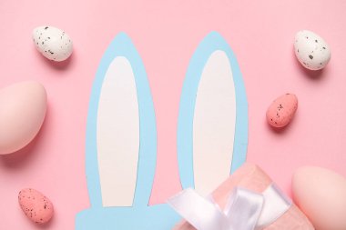 Paskalya yumurtaları ve pembe arka planda hediye kutusu olan kağıt tavşan kulakları.