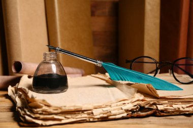 Ahşap zemin üzerinde kalem, mürekkep hokkası, bardak ve parşömenleri olan eski bir kitap.