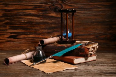 Ahşap zemin üzerinde kalem, mürekkep, parşömen ve kum saati olan eski kitaplar.