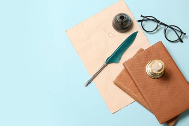 Kitaplı eski kağıt çarşaf, tükenmez kalem, mürekkep hokkası ve mavi arka planda gözlük.