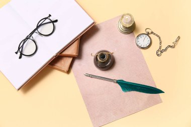 Kitaplı eski kağıt çarşaf, tükenmez kalem, mürekkep hokkası, gözlük ve bej arka planda cep saati.