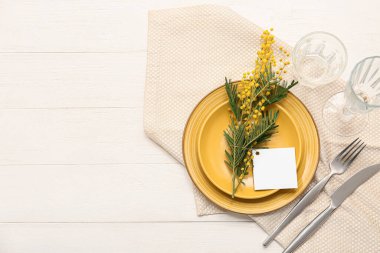 Boş kart ve beyaz ahşap arka planda mimoza çiçekleri olan güzel bir masa.