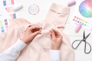 Beyaz ahşap masadaki bej gömlekli kadın dikiş düğmesi, üst manzara.