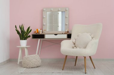 Ayna, koltuk, makyaj malzemesi ve makyaj masası olan şık bir makyaj odası.