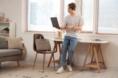 Bilgisayarı ve kulaklığı olan genç çocuk evde çalışıyor.