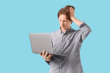 Bilgisayarlı kafası karışmış genç çocuk mavi arka plan üzerinde çalışıyor.