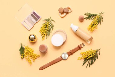 Kol saatli dekoratif kozmetik ürünler ve turuncu arka planda mimoza çiçekleri.