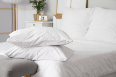 Beyaz battaniyeli rahat yatak ve şık yatak odasında yumuşak yastıklar, yakın çekim.