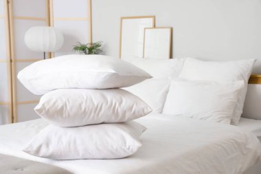 Beyaz battaniyeli rahat yatak ve şık yatak odasında yumuşak yastıklar, yakın çekim.