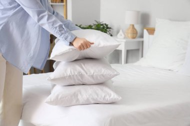 Yatak odasındaki yumuşak yastıkları istifleyen genç kadın, yakın plan.