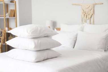 Beyaz battaniyeli rahat yatak ve şık yatak odasında yumuşak yastıklar, yakın çekim.