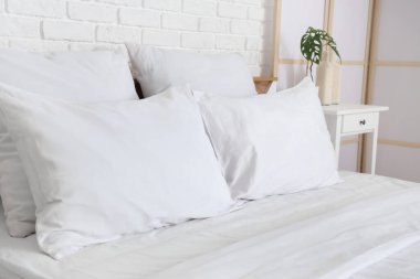 Beyaz battaniyeli rahat yatak ve şık yatak odasında yumuşak yastıklar, yakın çekim.