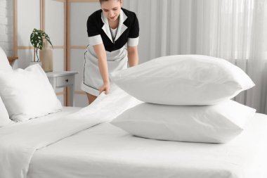Otel odasında yatak yapan genç ve güzel oda hizmetçisi, bir yığın yumuşak yastığa odaklan.