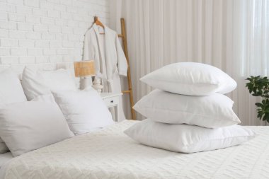 Beyaz battaniyeli rahat yatak ve şık yatak odasında bir yığın yumuşak yastık.