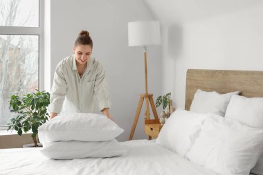 Yatak odasındaki yumuşak yastıkları istifleyen güzel genç bir kadın.