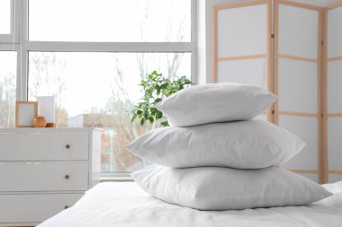 Beyaz battaniyeli rahat yatak ve şık yatak odasında yumuşak yastıklar, yakın çekim.