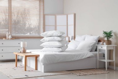 Beyaz battaniyeli rahat yatak ve şık yatak odasında bir yığın yumuşak yastık.