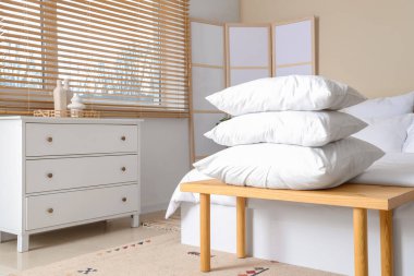 Beyaz battaniyeli rahat bir yatak ve şık bir yatak odasında, ahşap yatak başucunda bir yığın yumuşak yastık.