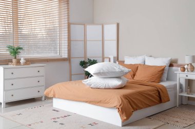 Kahverengi battaniyeli rahat yatak ve şık yatak odasında bir yığın yumuşak yastık.