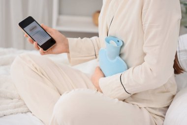 Yatak odasında adet takvimi kullanan telefonu olan genç bir kadın.