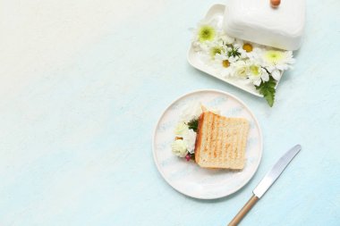 Kızarmış ekmek tabağı, tereyağı tabağı ve açık mavi arka planda güzel çiçekler.