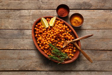 Ahşap arka planda biberiye, limon ve baharatlı bir kase lezzetli nohut.