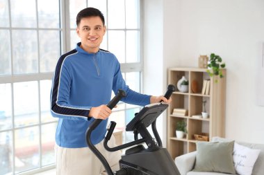 Sportif genç adam evde modern egzersiz bisikleti eğitimi alıyor.