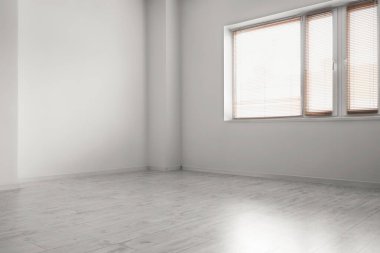 Beyaz duvarları, ahşap zemini ve penceresi olan boş bir odanın içinde.