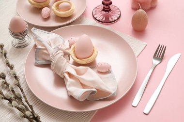 Beautiful table setting with Easter eggs and pussy willow branches on pink background, closeup