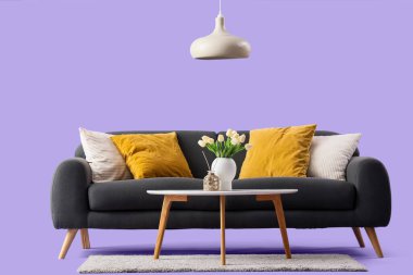 Mor arka planda yastıkları, sehpası ve lambası olan rahat siyah bir kanepe.